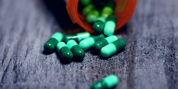 Prescribed medicine capsules spilling out from an open plastic pill container.