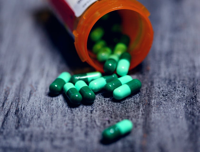 Prescribed medicine capsules spilling out from an open plastic pill container.