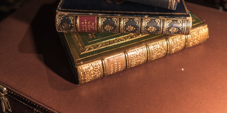 Stack of old books on top of a briefcase with bookshelves in the background.