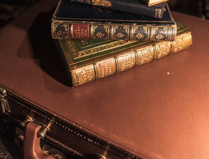 Stack of old books on top of a briefcase with bookshelves in the background.
