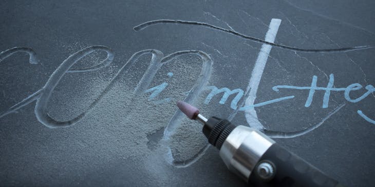 A dark slab of stone being engraved by an electric tool.