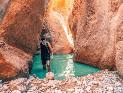 Un homme marchant dans l'eau bleue entre les hautes parois du canyon.