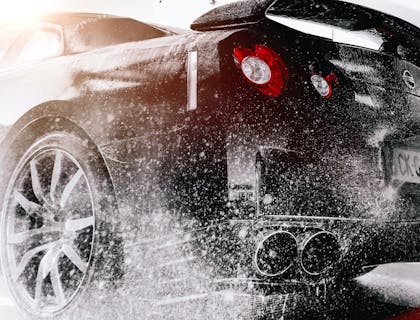 Black car washed at a car wash with a high pressure nozzle.