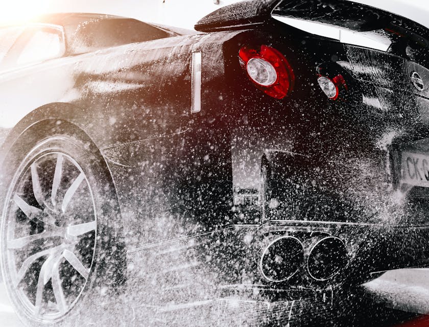 Black car washed at a car wash with a high pressure nozzle.