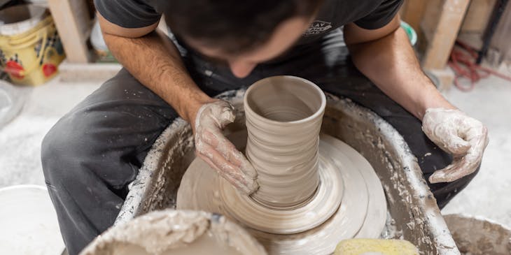 Person shaping a ceramic vase on a pottery wheel.