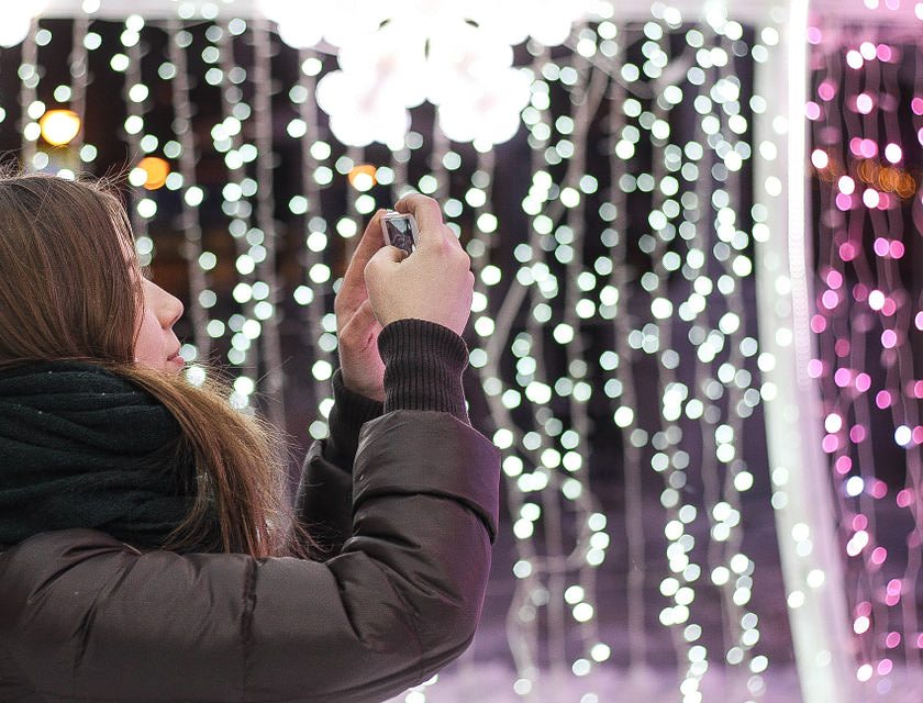 Una mujer con chaqueta café instalando luces navideñas de diferentes colores en un negocio de instalaación de luces navideñas.