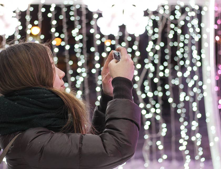 Una mujer con chaqueta café instalando luces navideñas de diferentes colores en un negocio de instalaación de luces navideñas.