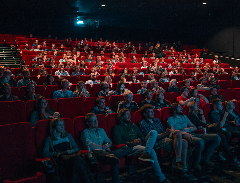 Delle persone sedute sulle poltrone rosse di un cinema che vogliono vedere un film.