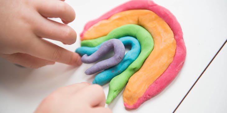 A toddler's hands creating a clay dough rainbow.