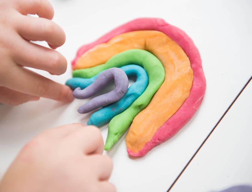 A toddler's hands creating a clay dough rainbow.