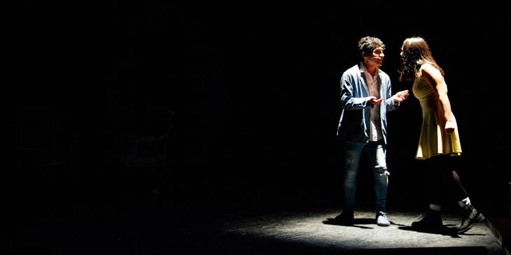 Two stage actors performing a drama scene under the spotlight in a theater.