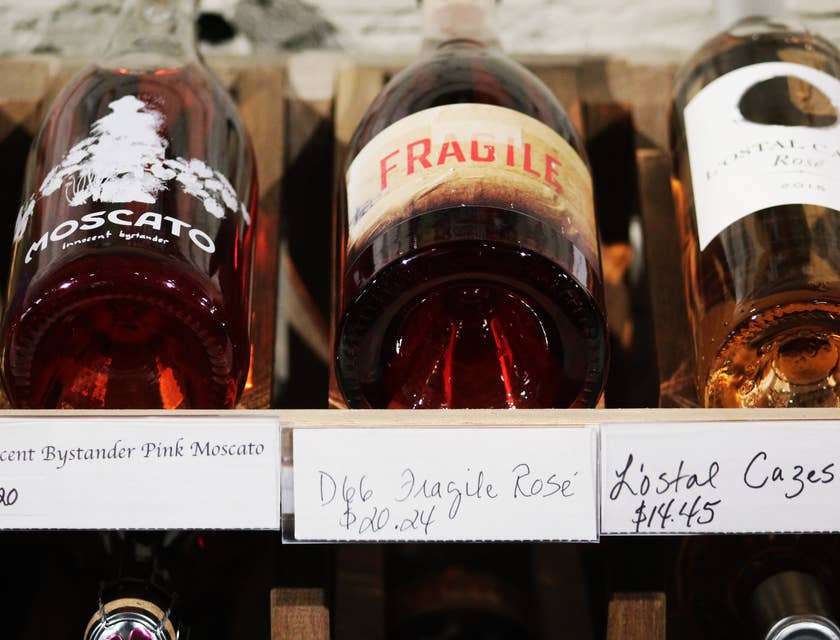 Três garrafas de bebida alcoólica com etiquetas de preços manuscritas em uma loja de bebidas alcoólicas.