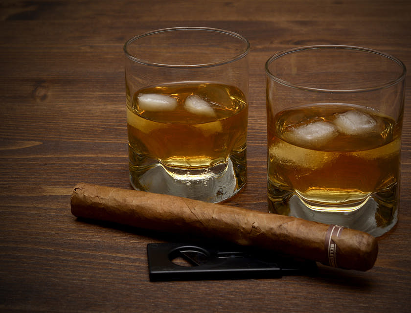 un puro sobre una mesa de madera oscura junto a un par de vasos de vidrio con whiskey y hielo en un bar de puros