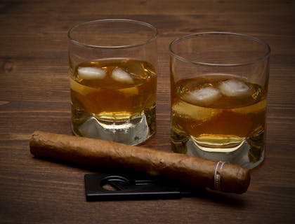Due bicchieri di whiskey e un sigaro cubano appoggiati sopra il tavolo di una cigar room.