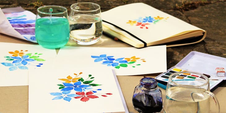 Colorful watercolor paintings of flowers spread out on a table at the end of a paint and sip class.