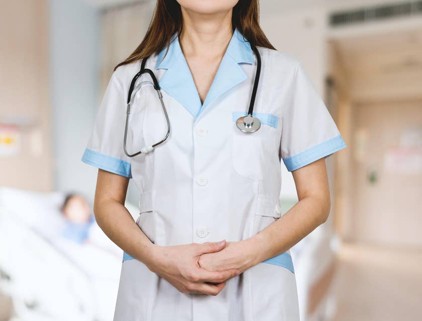 Eine Mitarbeiterin eines Krankenhauses mit einem Stethoskop trägt ihre weiße Arbeitskleidung, die mit hellblauen Rändern an den Armen und am Halsausschnitt abgesetzt ist.