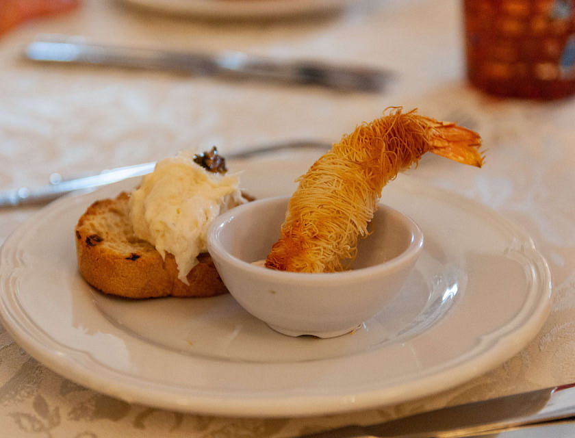 Crostino con baccalà mantecato e un gambero fritto in un piatto in un ristorante veneto.