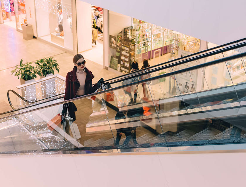 Una donna elegante sulle scale mobili di un outlet con in mano delle shopping bag.