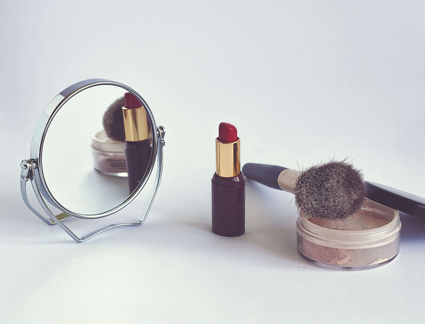 Alcuni trucchi, un pennello da trucco e uno specchio posizionati sopra il bancone di una profumeria.