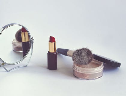 Alcuni trucchi, un pennello da trucco e uno specchio posizionati sopra il bancone di una profumeria.