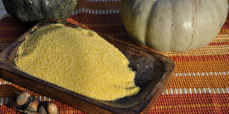 Farina di mais per polenta su un piatto bianco con delle zucche sullo sfondo.