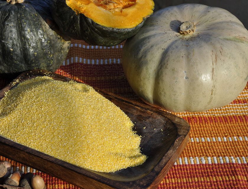 Farina di mais per polenta su un piatto bianco con delle zucche sullo sfondo.