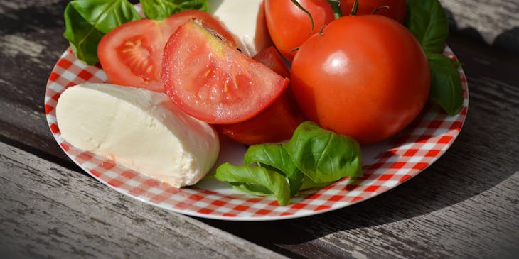 Pomodoro, mozzarella e basilico su un piatto. a quadretti rosso e bianco posto sopra un tavolo di legno.