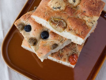 Tre fette di focaccia pugliese in un piatto marrone sopra un tavolo con una tovaglia bianca.