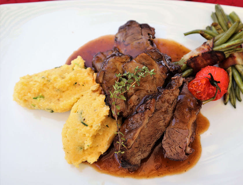Polenta e brasato di carne serviti su un piatto bianco in un ristorante valdostano.