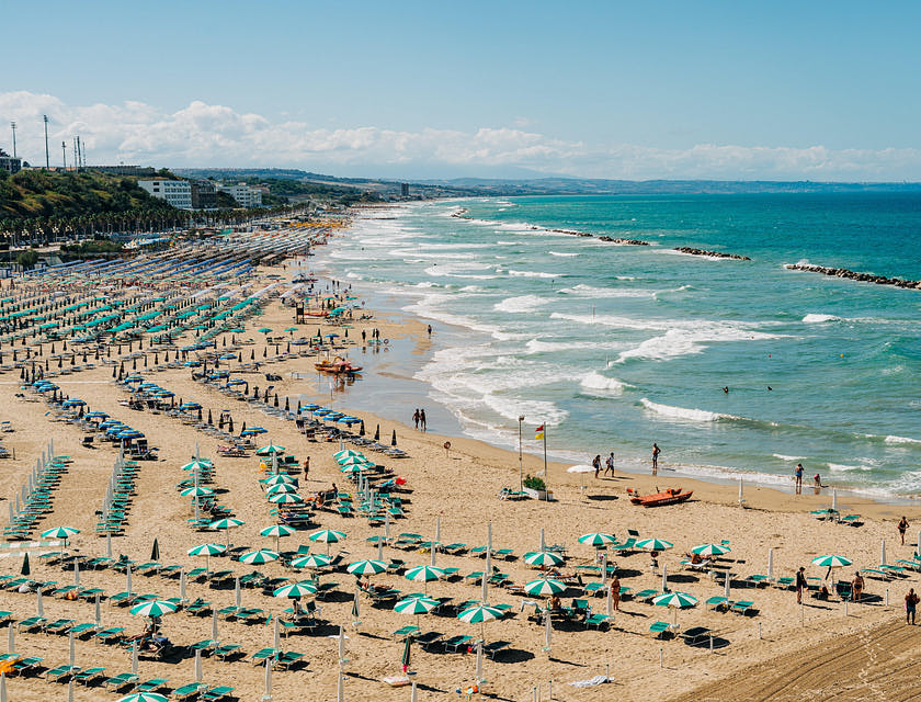 Uno stabilimento balneare con ombrelloni e sdraio blu e azzurre situato in un'ampia spiaggia con mare blu cristallino.