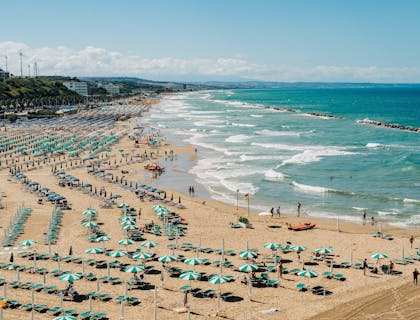 Uno stabilimento balneare con ombrelloni e sdraio blu e azzurre situato in un'ampia spiaggia con mare blu cristallino.