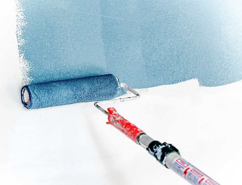 Capa de pintura azul que se aplica a una pared blanca con un rodillo en un negocio de pintura.
