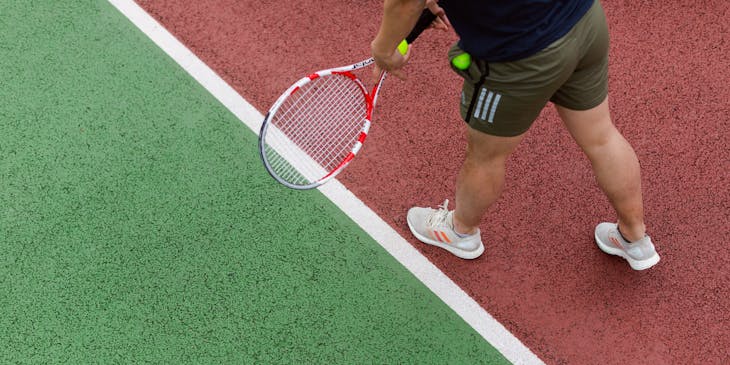 Tennis coach with a tennis racket and ball demonstrating a serve.