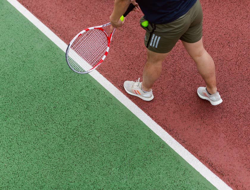 Un istruttore di tennis che impugna una racchetta e una pallina che mostra a uno studente come si fa un servizio sul campo da tennis.