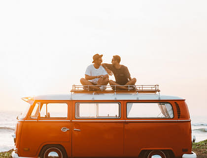 Two chilled people sitting on the roof of a camper van.