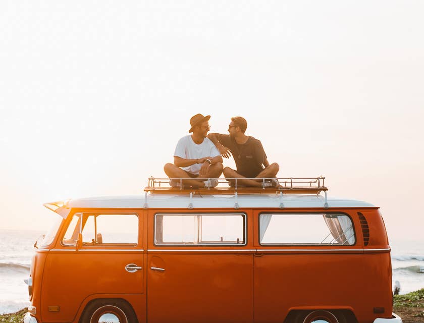 Two chilled people sitting on the roof of a camper van.