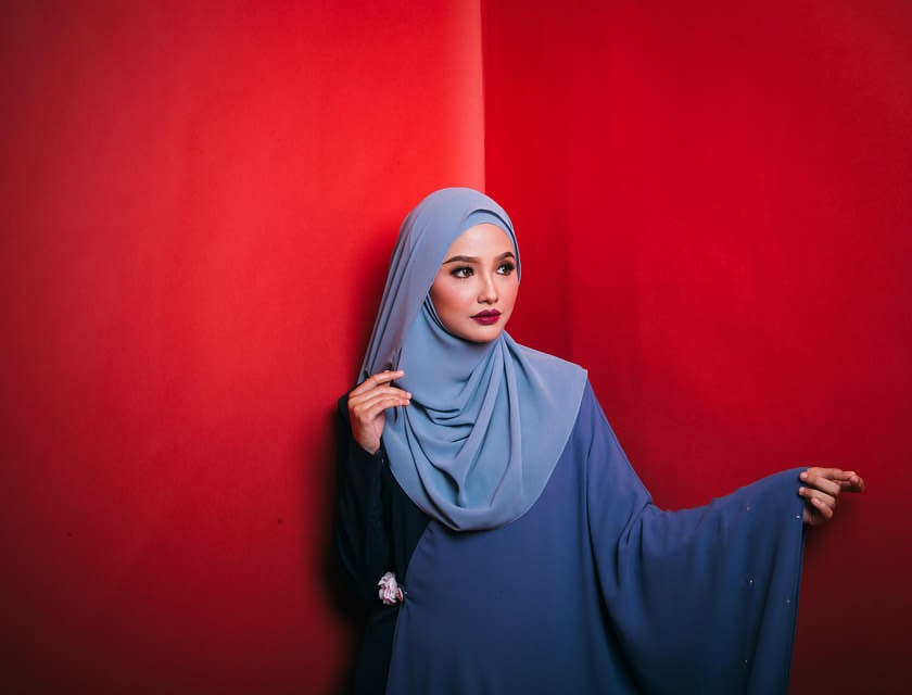 Mulher usando hijab azul em frente a uma parede vermelha.