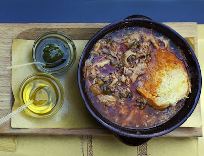 Un coccio di lampredotto e trippa al pomodoro con salsa verde e pane in una tripperia.