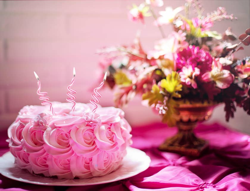 Ein rosa Kuchen auf einem Teller liegt auf einem Tisch, der mit einer pinken Tischdecke und einem Plastikblumenstrauß eines Dekoladens dekoriert ist.