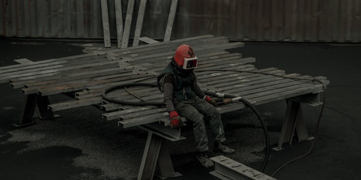 A sandblasting technician sitting in steel rods.