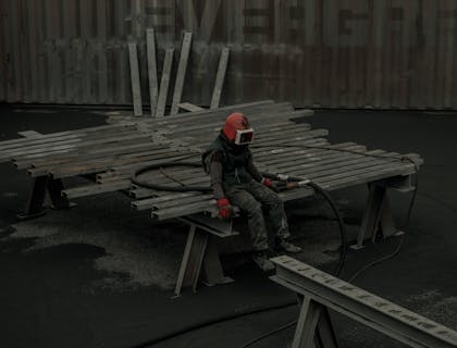 A sandblasting technician sitting in steel rods.