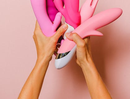 Person holding several pink sex toys.