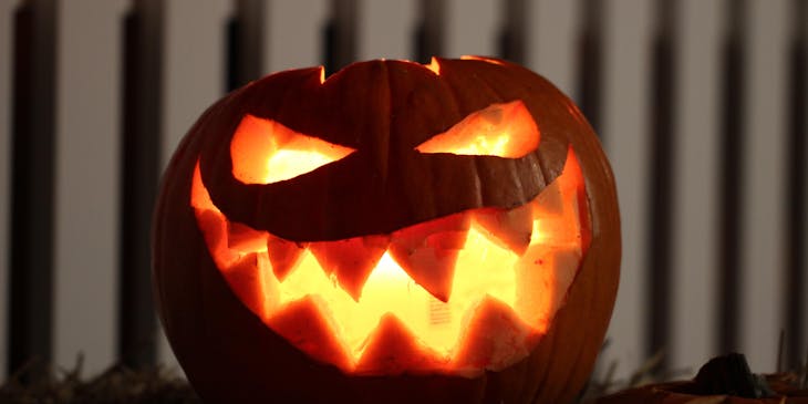 A spooky Jack-o-lantern in front of a white picket fence.