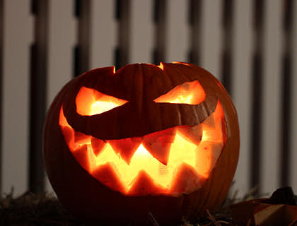 A spooky Jack-o-lantern in front of a white picket fence.