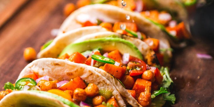 A taco truck chef adding the finishing touches to a tray of tacos.