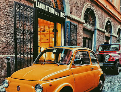Una cinquecento gialla d'epoca, appena restaurata, parcheggiata in una strada antica.