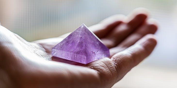 A purple pyramid-shared crystal being held in an alternative healing center.
