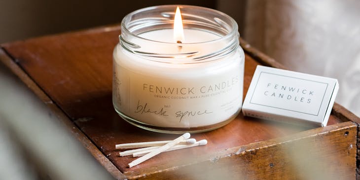 Una vela perfumada blanca ardiendo en un frasco de vidrio sobre una mesa en un negocio de velas.