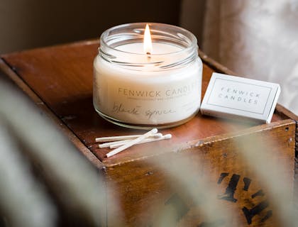 Una vela perfumada blanca ardiendo en un frasco de vidrio sobre una mesa en un negocio de velas.