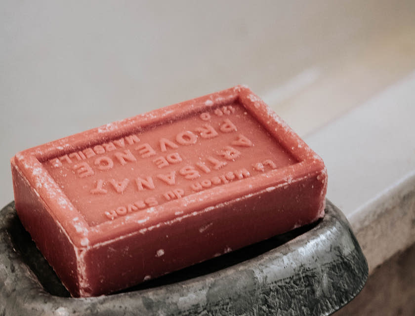 Artisan soap bar in a soap holder on the edge of a bathtub.